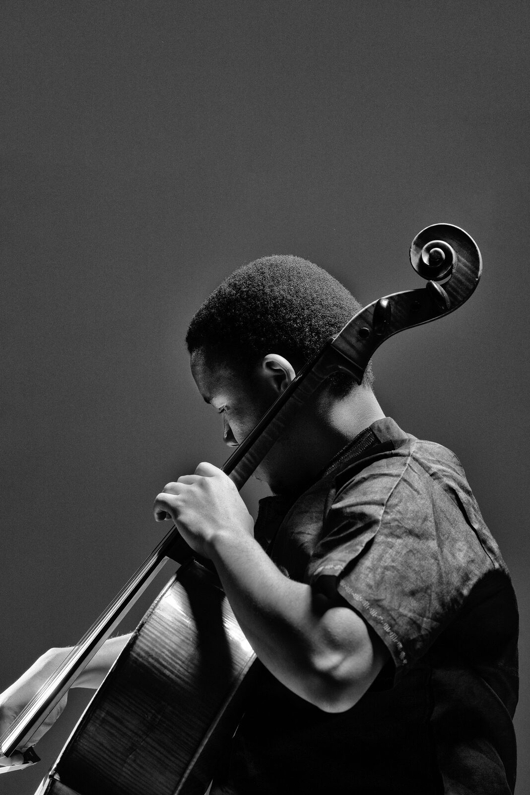 Black-and-white portrait of a cellist leaning into the instrument against a plain dark background.